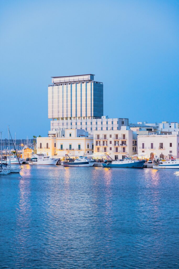 Scenic view of Gallipoli's harbor with luxury yachts and a modern skyscraper at dawn.